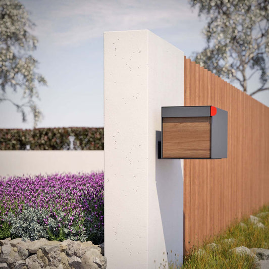 Post mount mailbox TOWN SQUARE in anthracite with wood panel installed as a residential mailbox beside a garden fence.